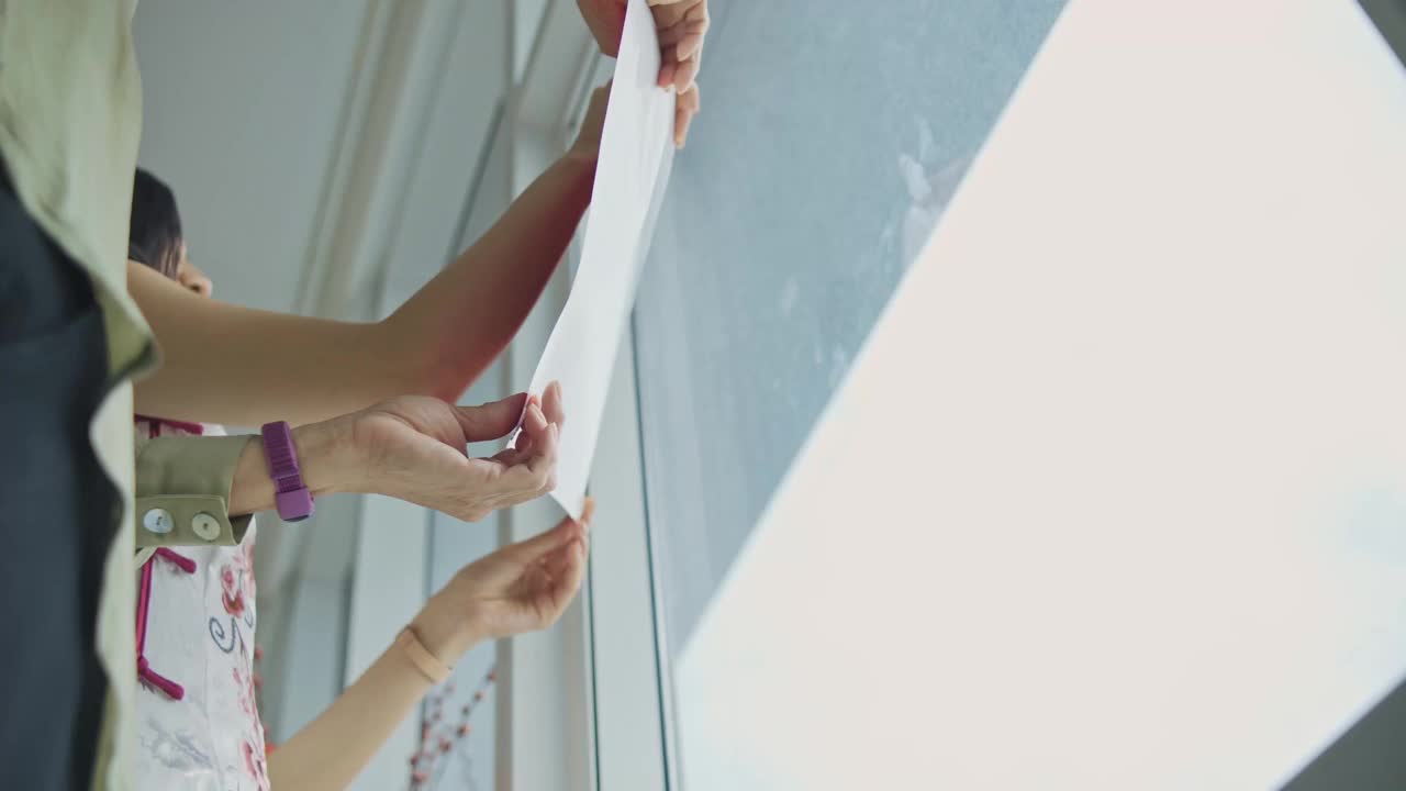 低角度看中国新年高级妇女和她的女儿装饰房子客厅与中国文字书法装饰在窗户上准备家庭团聚