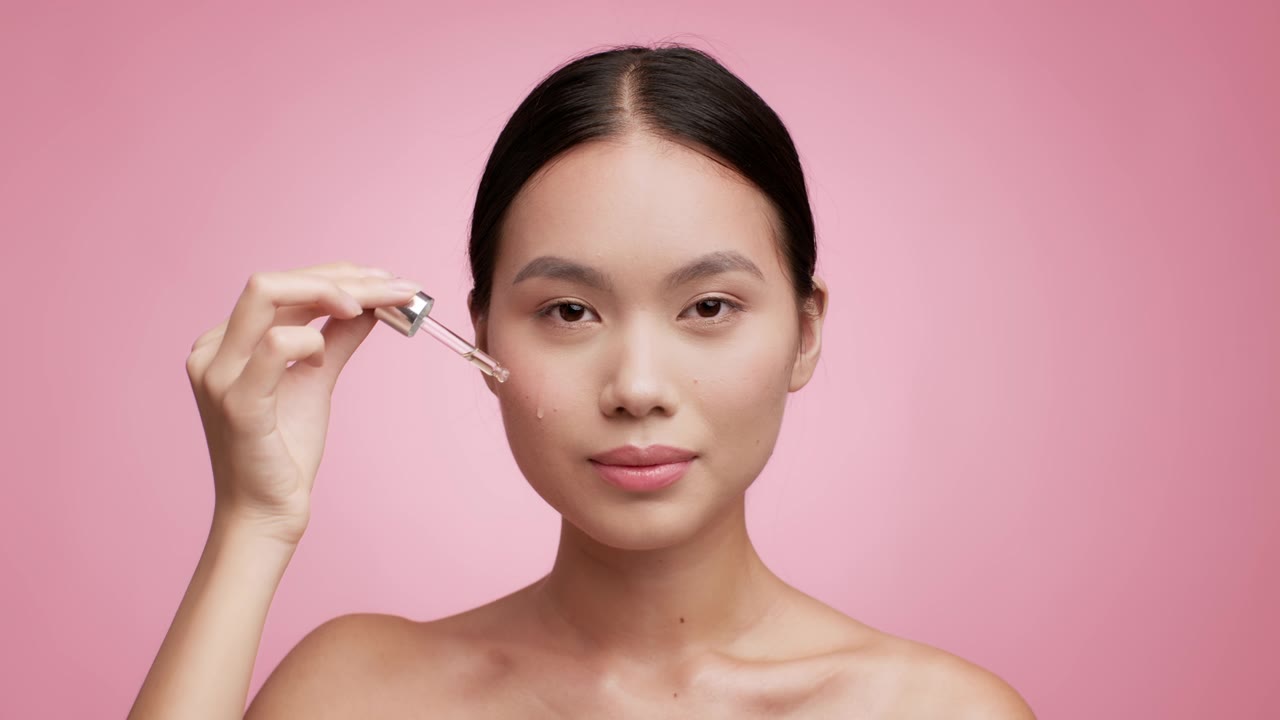 詳情圖-亞洲女性使用滴管在粉紅色背景上使用面部精華液