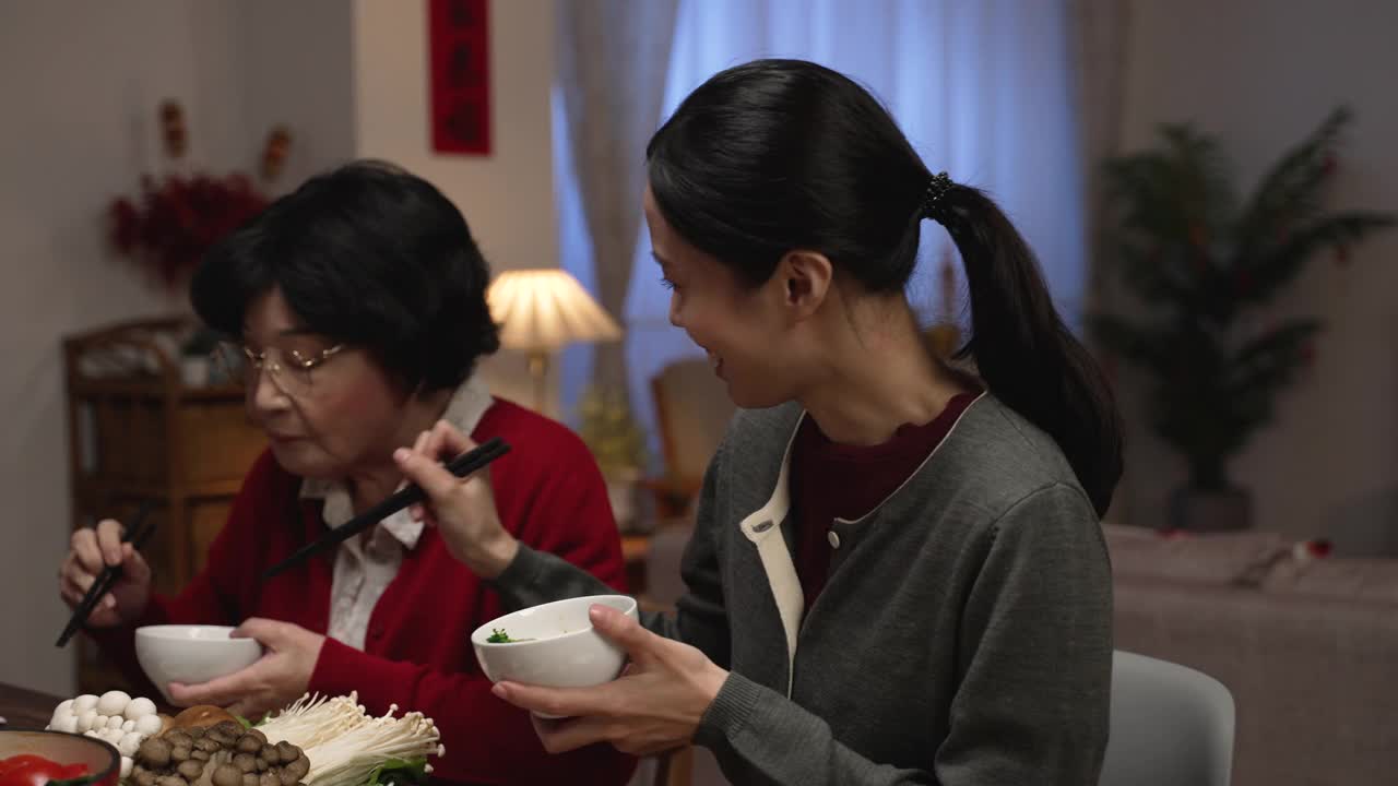 快乐的亚洲媳妇在和她穿着红色衣服的老母亲聊天，他们在家里享受丰盛的年夜饭。