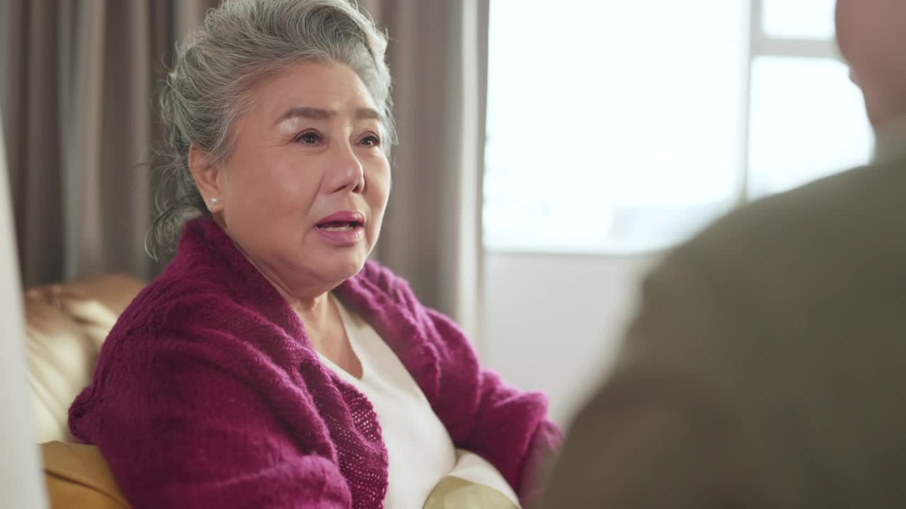 幸福亚洲成年退休女性休闲服饰放松坐在沙发沙发上与家人聊天交谈假期周末客厅，亚洲老年女性与家人良好的关系留在家里呆在家里