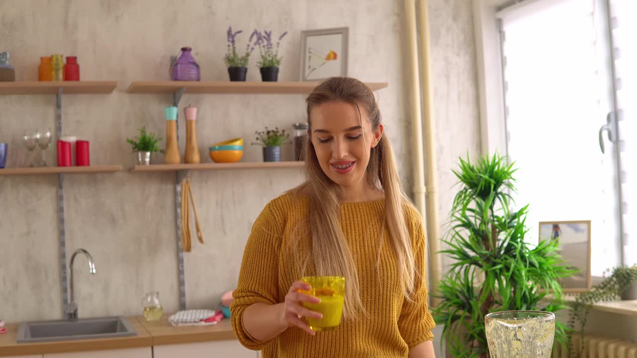 美丽的年轻女子喜欢喝一种健康的水果奶昔，这是她在厨房用搅拌机做的
