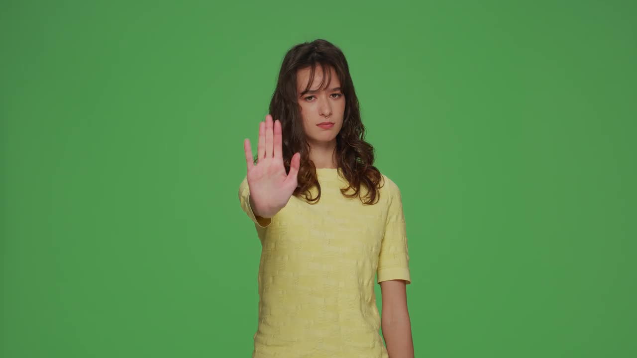 严肃的年轻女孩显示停止手势，抗议，否认，警告，禁止在彩键绿色工作室背景