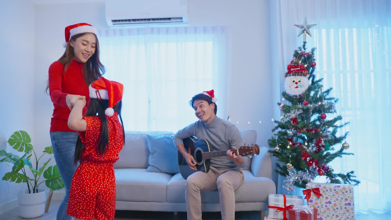 亚洲可爱的家庭成员在家里一起享受唱圣诞歌。年幼的女儿兴高采烈地在家里和父母一起庆祝节日圣诞感恩节派对。