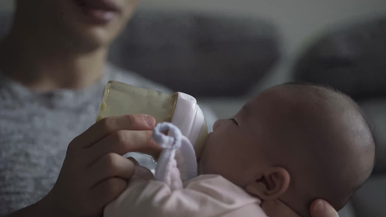 亚洲华人年轻的父亲在周末在客厅用奶瓶喂他的儿子