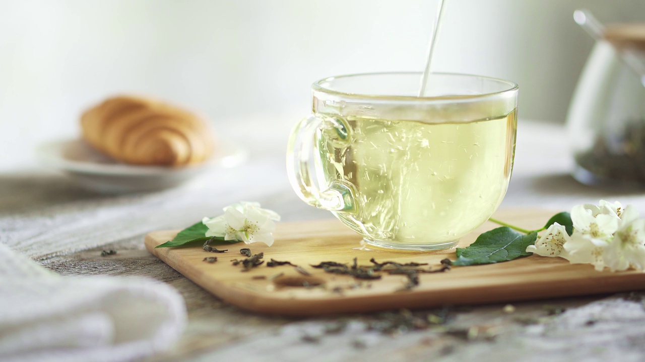 一杯茉莉花茶在玻璃杯中喷涌而出。透明杯，竹板，茉莉花枝