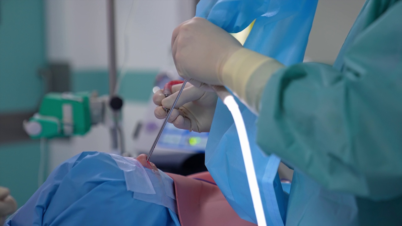 外科医生的手对患者进行耳鼻咽喉手术。鼻中隔成形术在现代手术室中的表现。医生把医疗器械放进病人的鼻子里。