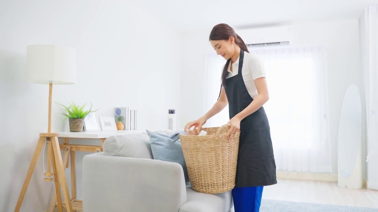 詳情圖-亞洲清潔服務女工清潔客廳在家里。漂亮的年輕女孩管家清潔工感到高興，并把臟臟的衣服放進籃子里做家務或家務。