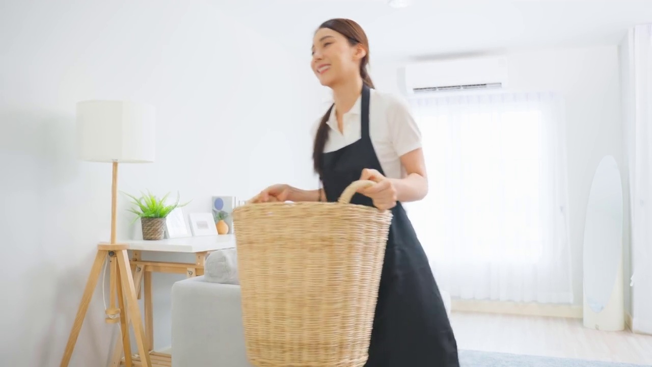 詳情圖-亞洲清潔服務女工清潔客廳在家里。漂亮的年輕女孩管家清潔工感到高興，并把臟臟的衣服放進籃子里做家務或家務。