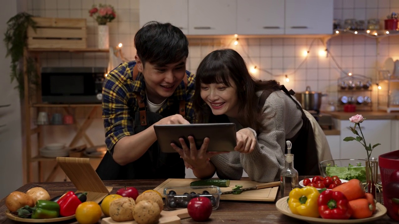 詳情圖-幸福的亞洲夫婦一起使用電子平板，在網(wǎng)上瀏覽食譜，討論在家里的廚房做什么情人節(jié)晚餐