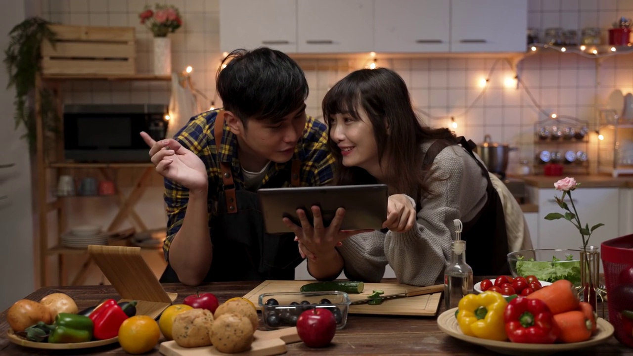 詳情圖-幸福的亞洲夫婦一起使用電子平板，在網(wǎng)上瀏覽食譜，討論在家里的廚房做什么情人節(jié)晚餐
