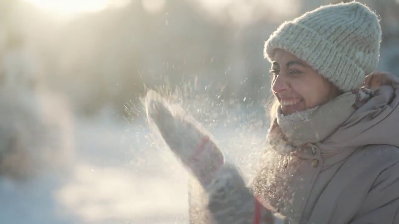 详情图-慢动作:年轻女子吹雪。在霜冻的冬日里，一个有趣的女孩在冬季公园里从手套里吹雪。快乐兴奋的女孩，享受着霜冻的新鲜，玩着新鲜的雪