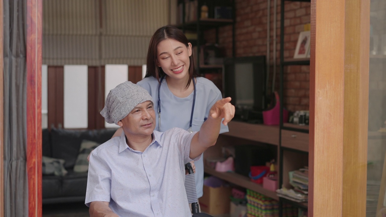 年轻的亚裔护士正在与癌症患者交谈并鼓励他们。患有癌症的亚裔老人坐在轮椅上，戴着一块大手帕来掩盖化疗时脱发的情况。