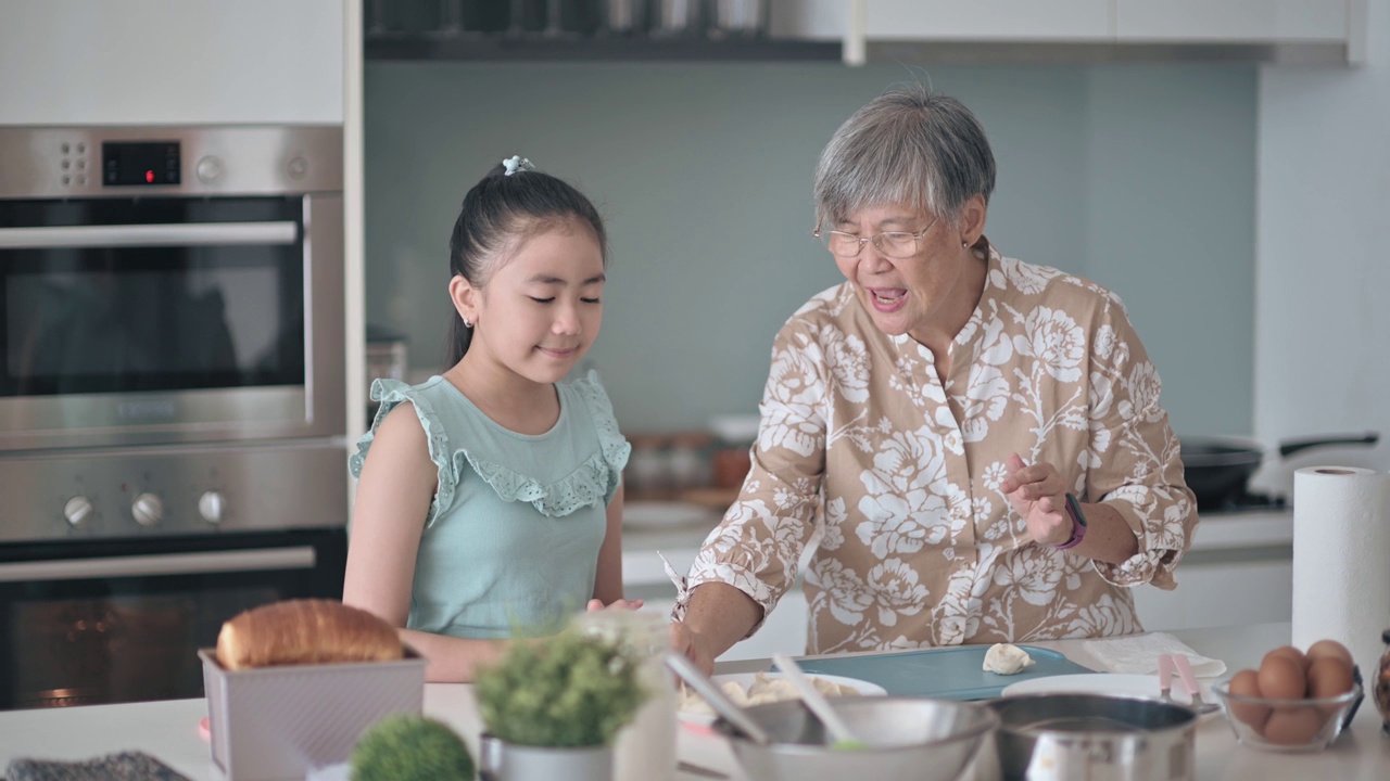 亚裔华人老太太周末在厨房展示和教她的孙女煮饺子