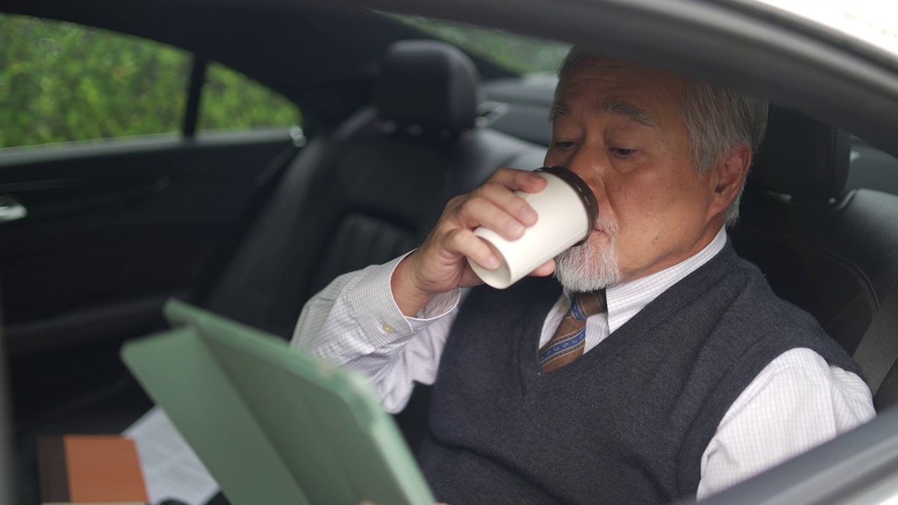 詳情圖-4K亞洲資深商人坐在汽車后座，一邊喝著熱咖啡，一邊在數(shù)碼平板電腦上工作