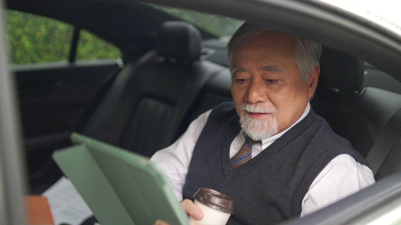 詳情圖-4K亞洲資深商人坐在汽車后座，一邊喝著熱咖啡，一邊在數(shù)碼平板電腦上工作