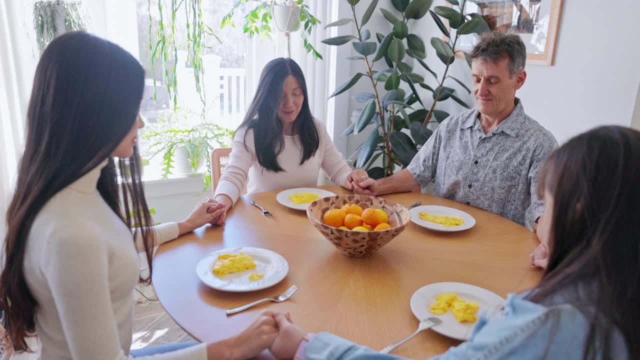 不同的家庭在早餐前在餐桌上祈祷。一个女儿患有唐氏综合症