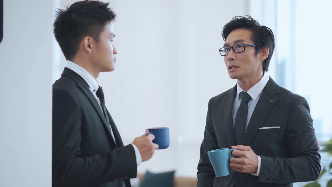 2名亚洲华裔白领西装革面，在办公室走廊喝酒休息