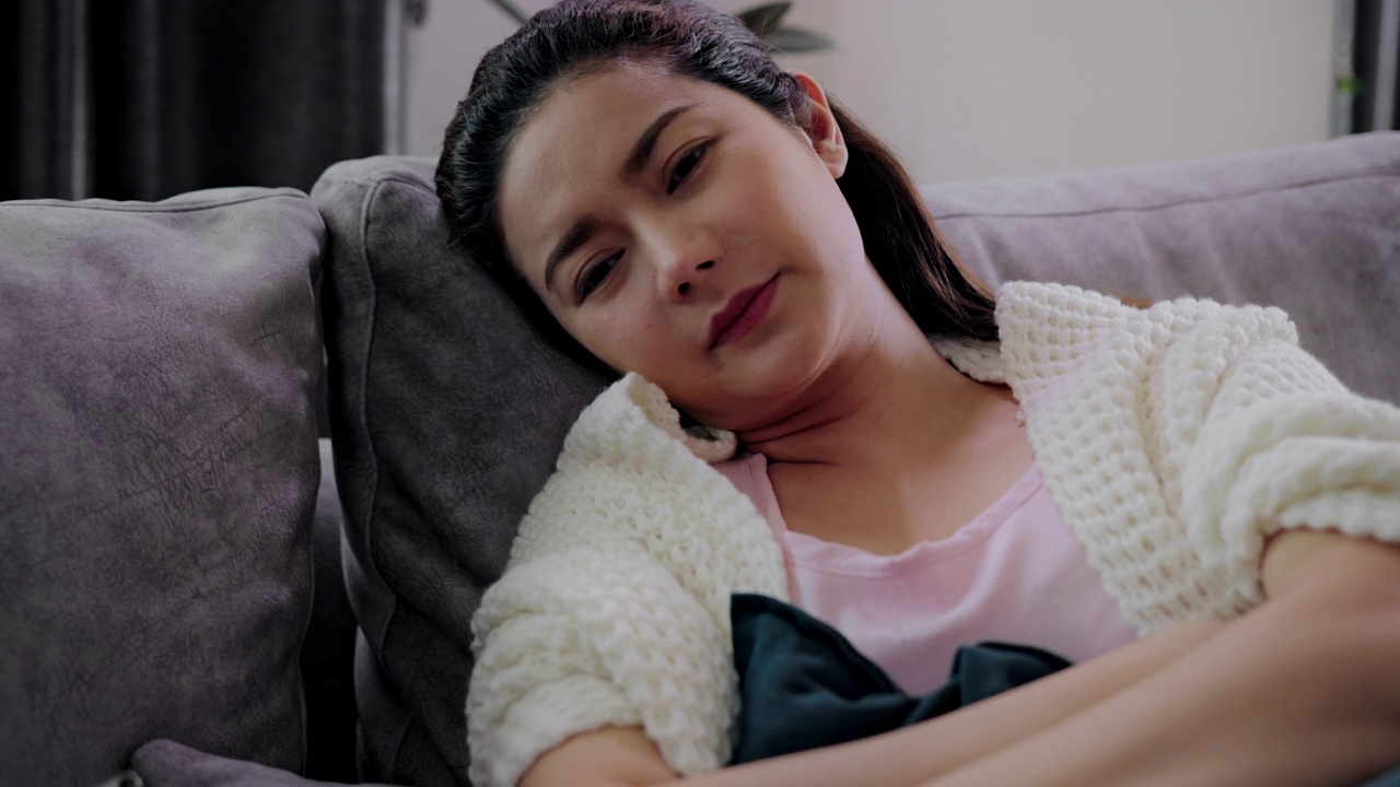 亚洲生病的自由职业妇女与高烧躺在沙发上感觉强烈的头痛在家里。疾病季节性病毒问题感冒和偏头痛。
