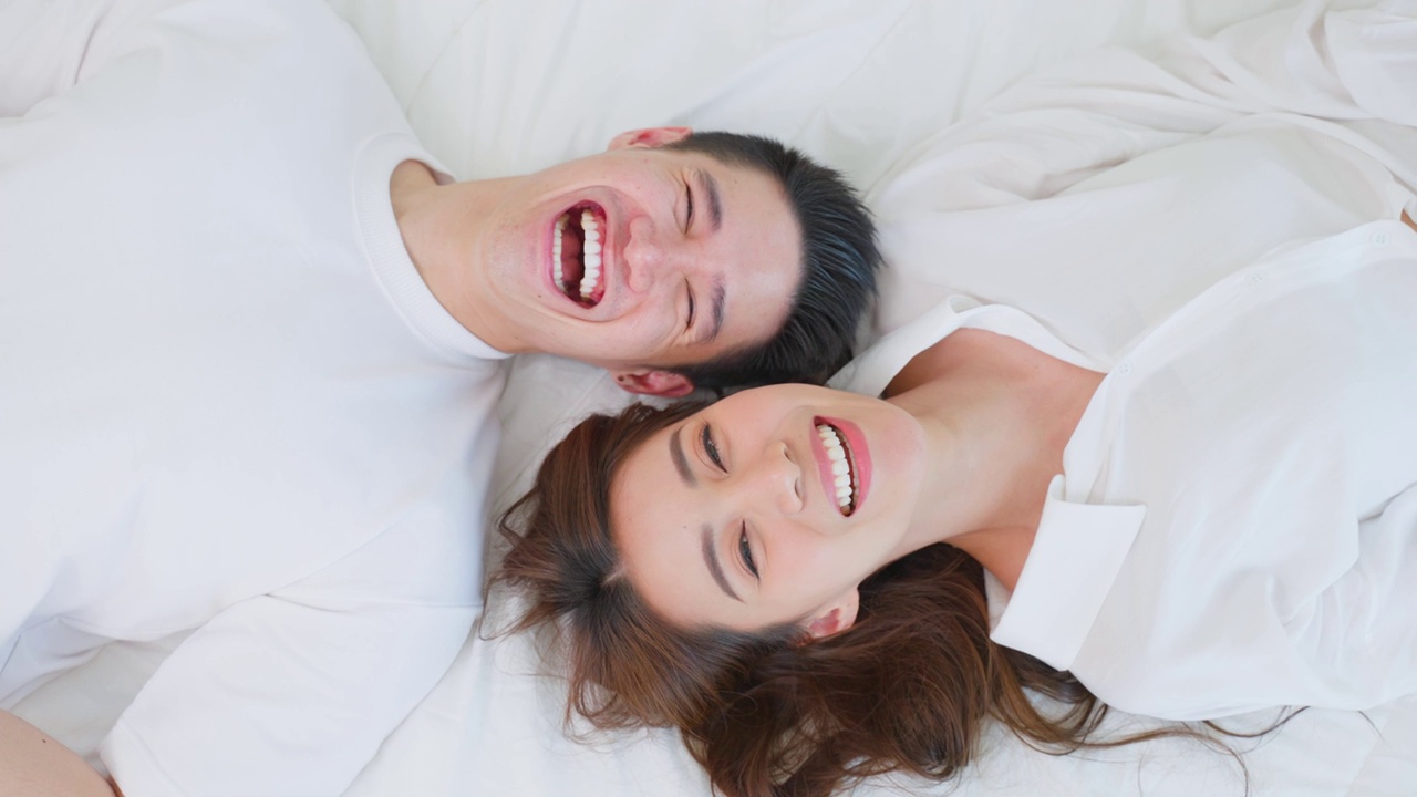 详情图-亚洲新婚夫妇躺在床上看着相机的肖像。漂亮漂亮的年轻男女穿着睡衣在家里的卧室里享受清晨的活动。关系的概念