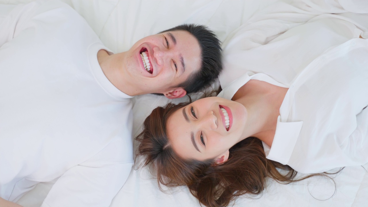 详情图-亚洲新婚夫妇躺在床上看着相机的肖像。漂亮漂亮的年轻男女穿着睡衣在家里的卧室里享受清晨的活动。关系的概念