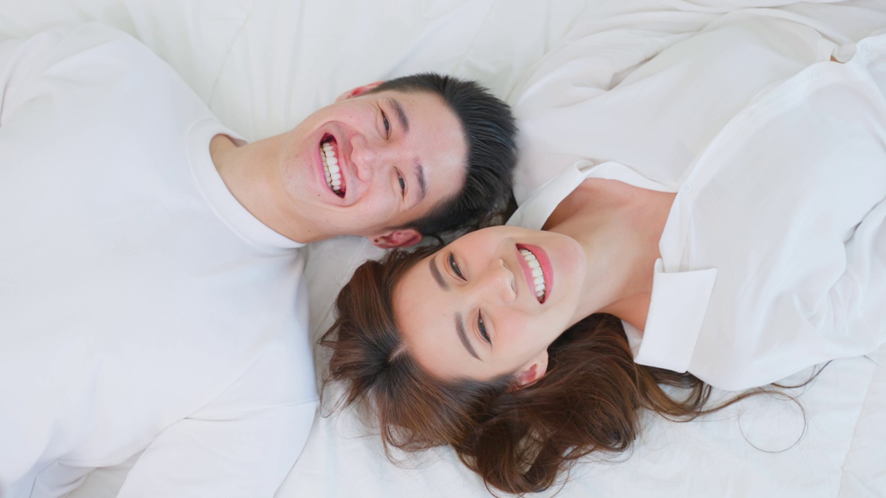 详情图-亚洲新婚夫妇躺在床上看着相机的肖像。漂亮漂亮的年轻男女穿着睡衣在家里的卧室里享受清晨的活动。关系的概念