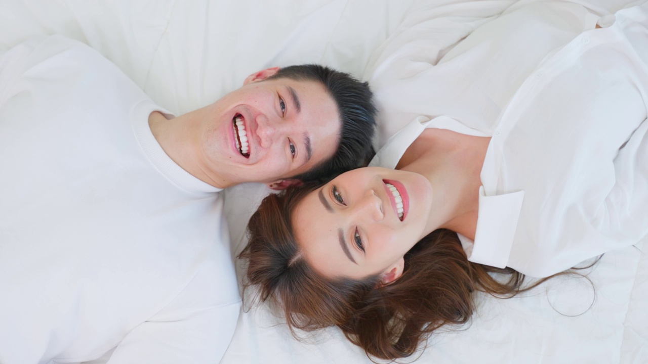 详情图-亚洲新婚夫妇躺在床上看着相机的肖像。漂亮漂亮的年轻男女穿着睡衣在家里的卧室里享受清晨的活动。关系的概念