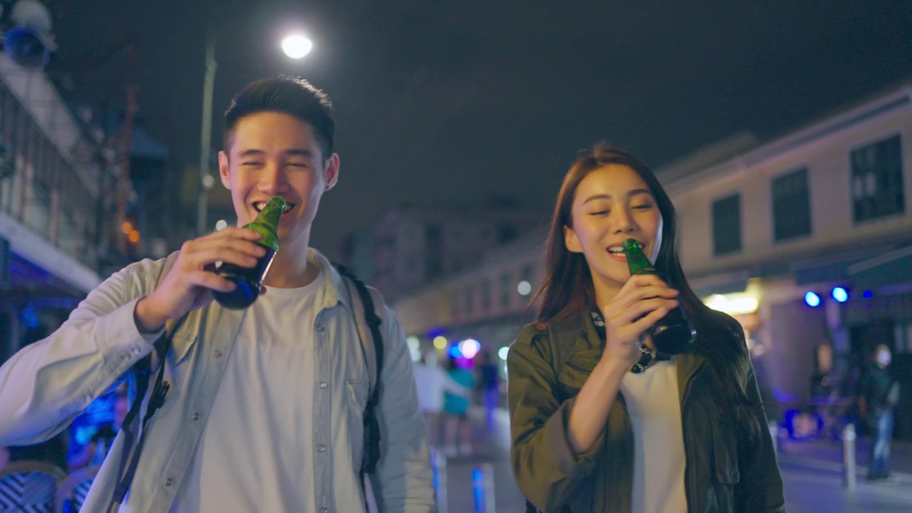 詳情圖-亞洲帥哥情侶一起喝酒開(kāi)派對(duì)。在城市里旅游的青年男女，在假期里一起拿著一瓶啤酒，在漆黑的夜晚在路上度過(guò)時(shí)光。
