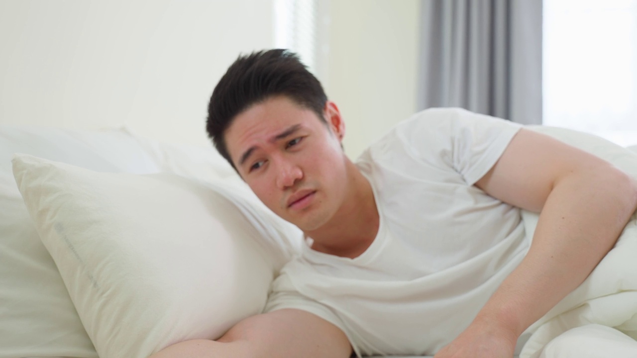 详情图-亚洲有魅力的年轻人关掉早上的闹钟。帅男觉得懒，累了躺在舒适的床上，在卧室里无视噪音，继续睡觉不想醒来