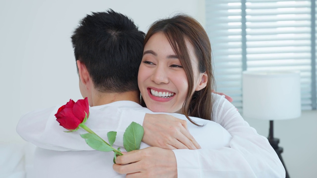 詳情圖-亞洲青年驚喜送玫瑰給美麗的女友。迷人浪漫的新婚男女坐在床上，一起享受慶祝周年紀(jì)念日和情人節(jié)