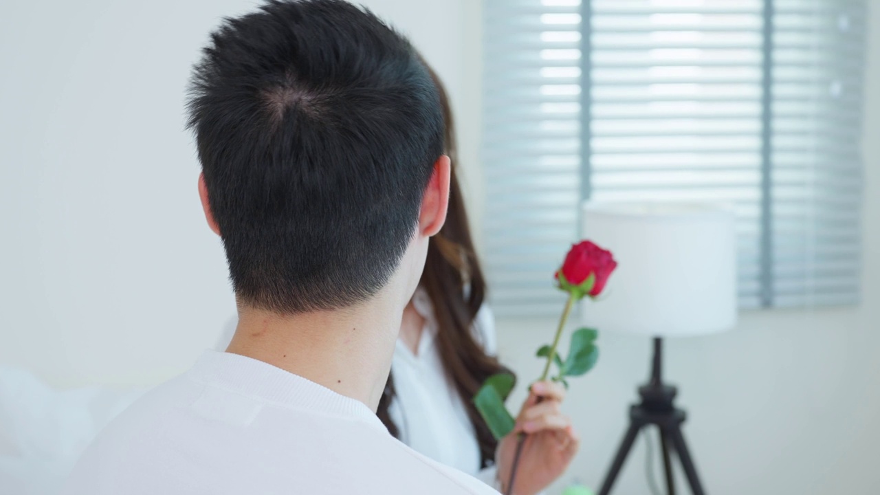 詳情圖-亞洲青年驚喜送玫瑰給美麗的女友。迷人浪漫的新婚男女坐在床上，一起享受慶祝周年紀(jì)念日和情人節(jié)