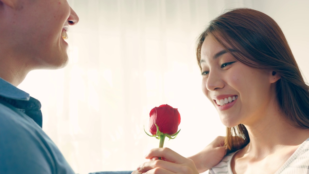 詳情圖-亞洲青年驚喜送玫瑰給美麗的女友。迷人浪漫的新婚男女花時間在房子里一起慶祝周年紀(jì)念日和情人節(jié)。