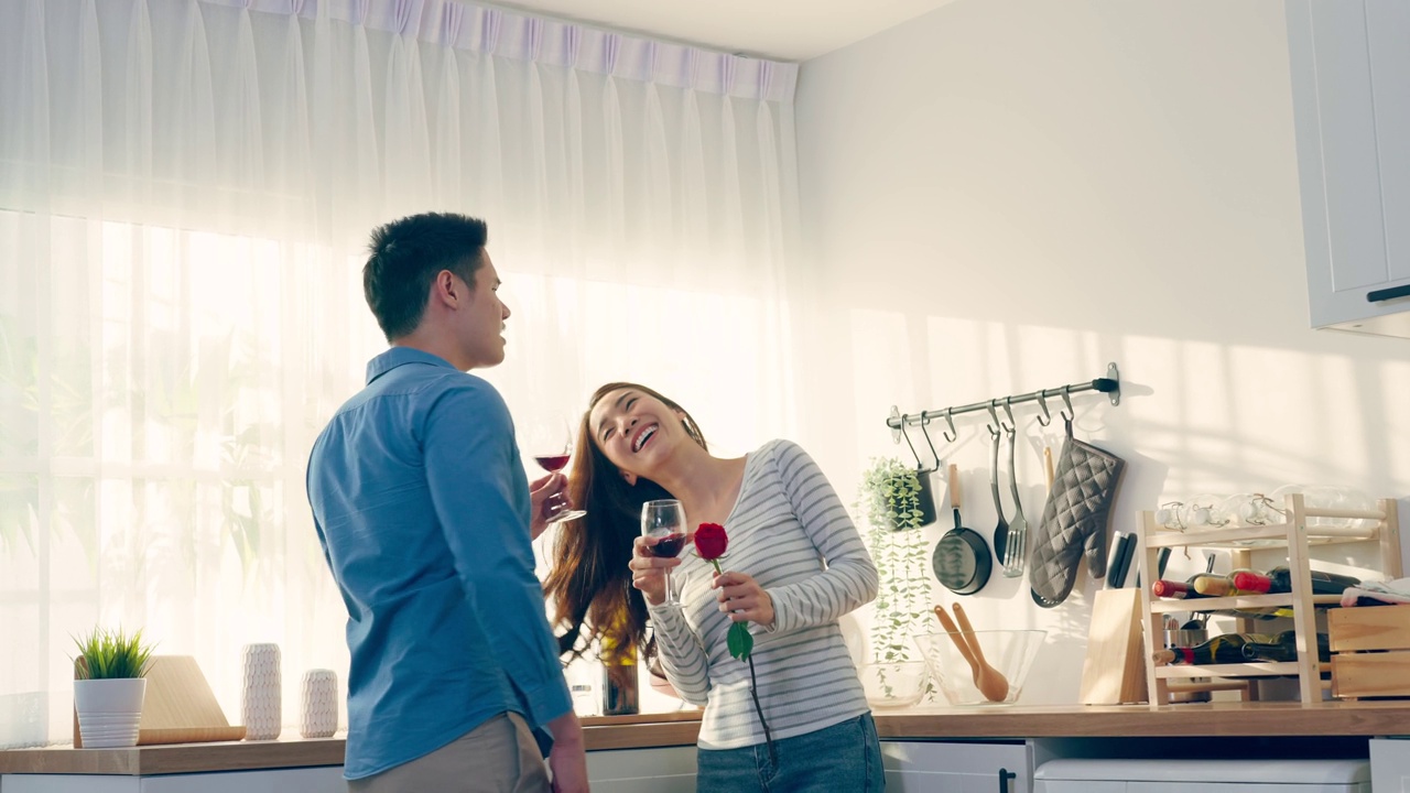 亚洲年轻情侣在情人节举杯畅饮。可爱浪漫的新婚男女在家里厨房共进晚餐庆祝结婚纪念日