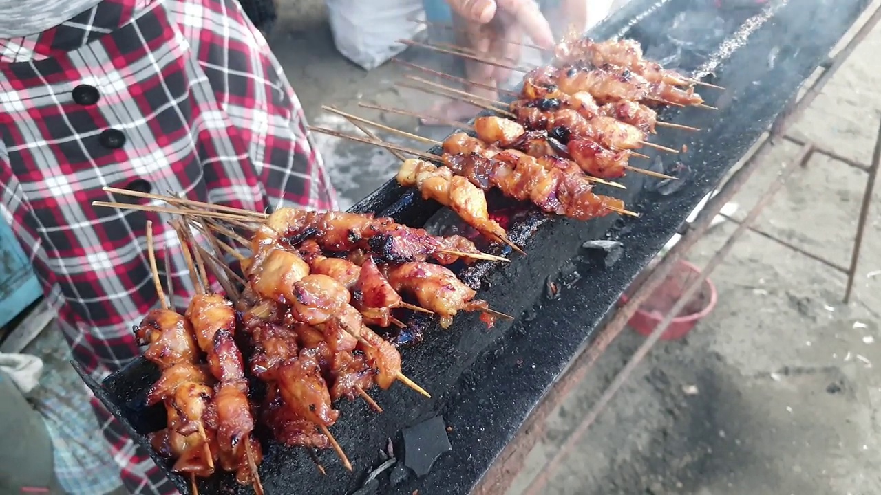 在沙滩上的户外长烤架上烤着沙爹鸡肉