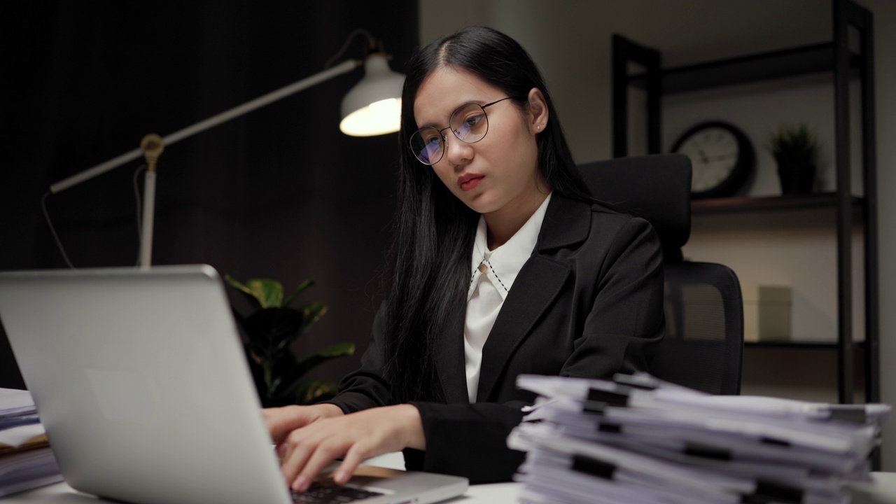 年轻的亚洲女商人工作到深夜。她忙着检查文件，不得不在截止日期前把工作发过去，感到压力很大。晚上坐在黑暗的办公室里。