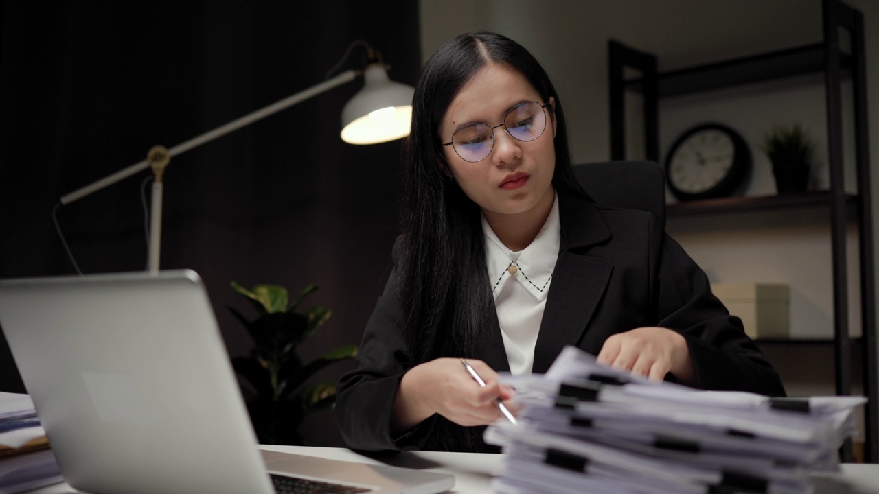 詳情圖-年輕的亞洲女商人工作到深夜。她忙著檢查文件，不得不在截止日期前把工作發(fā)過去，感到壓力很大。晚上坐在黑暗的辦公室里。