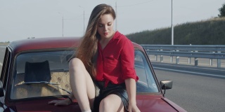 一位年轻女子正坐在一辆旧汽车的润滑油上。青春的乐趣和娱乐