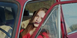 年轻迷人的女子坐在一辆开着门的旧车的前座上。的第一辆车