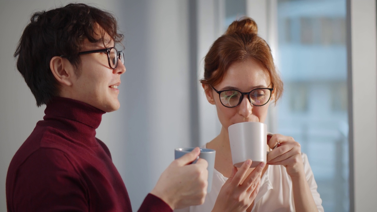 商务人士站在现代办公室的窗口，拿着咖啡杯微笑和交谈