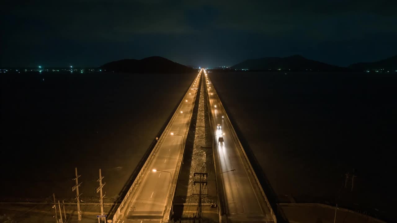 空中无人机Hyper Lapse或时间推移，夜间到白天的场景，交通车辆在跨越松卡湖，廷素拉暖达桥。沿着横跨泰国松卡湖的大桥
