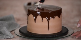 糕点师正用刀在蛋糕上涂上巧克力釉来装饰蛋糕。巧克力从两边流下来。