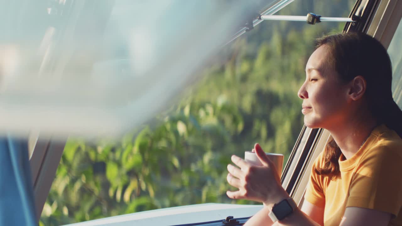 亞洲婦女感覺放松在露營(yíng)車喝咖啡的早晨與幸福和微笑的假期