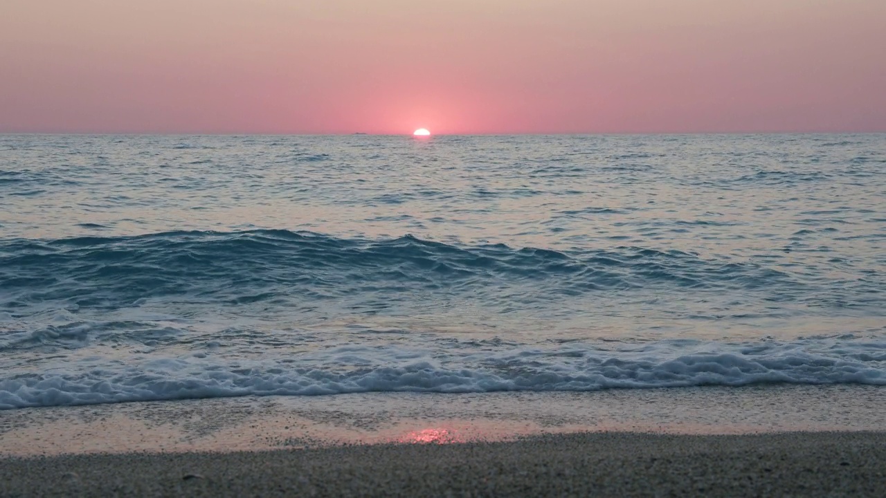 浪漫的海上日落背景。紫色的地平线上的天空没有云，海浪朝着卵石滩