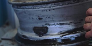 一名汽车修理工在安装轮胎时用密封胶涂抹汽车圆盘。
