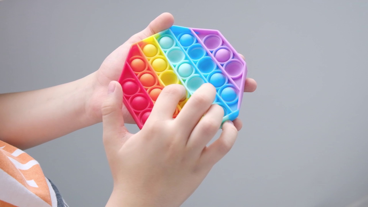 反应力的弹出它的玩具。特写镜头:孩子的手在玩彩虹感官游戏。彩色硅胶pop it玩具。