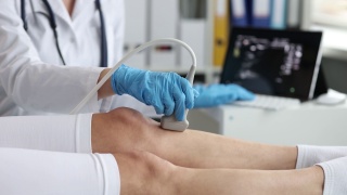 戴着橡胶手套的医生用超声波机扫描病人的腿
