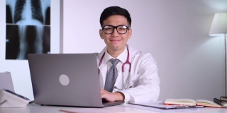 善良和礼貌的年轻亚洲医学医生，矫形外科医生，戴着听诊器，坐在笔记本电脑，直视x光图像背后的医院的检查室。