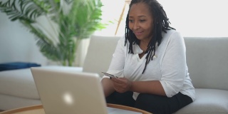 漂亮的黑人女人用笔记本电脑在家里的沙发上买东西的照片