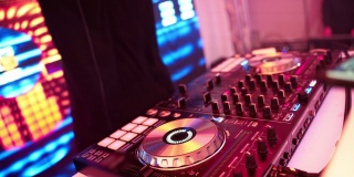 DJ的手在拧着DJ的遥控器上的不同按钮，俱乐部里的颜色和轻音乐。与dj派对