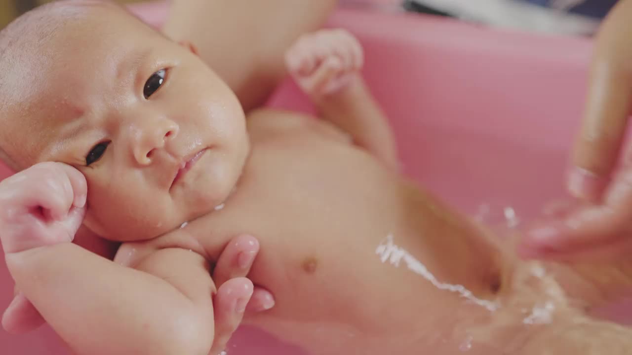 母亲给新生婴儿洗澡，背景是孤立的粉红色。