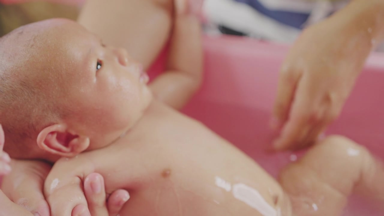 详情图-母亲给新生婴儿洗澡，背景是孤立的粉红色。